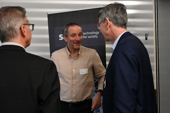 Three men talking in front of a technology banner.